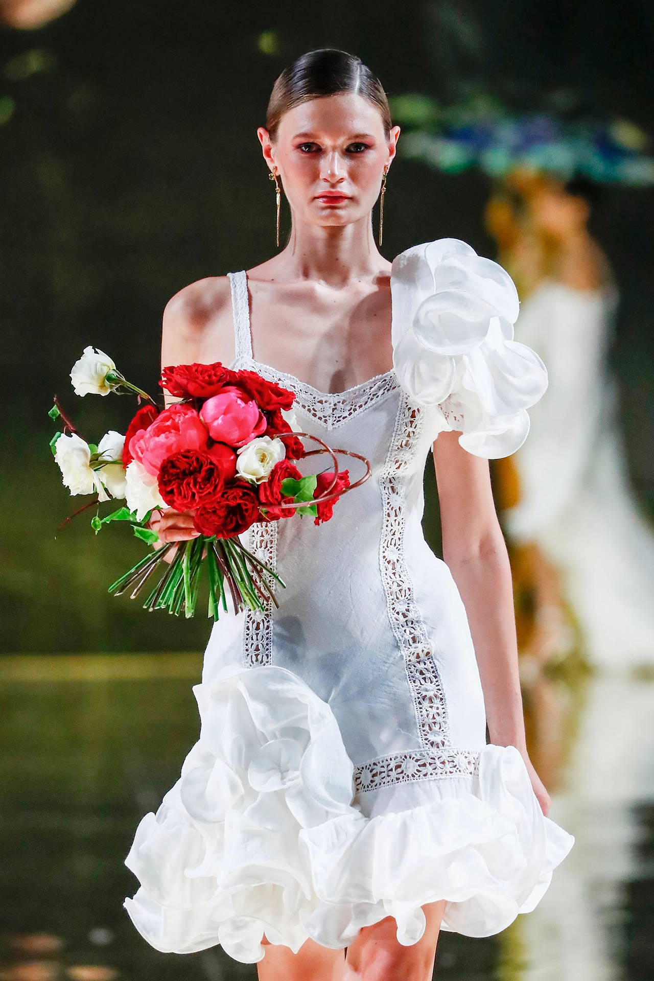 Modelo con vestido corto blanco de volantes y puntilla con ramo rojo